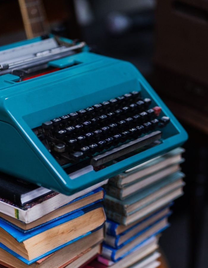 A turquoise typewriter sits atop a stack of vintage books, creating a nostalgic and creative vibe.